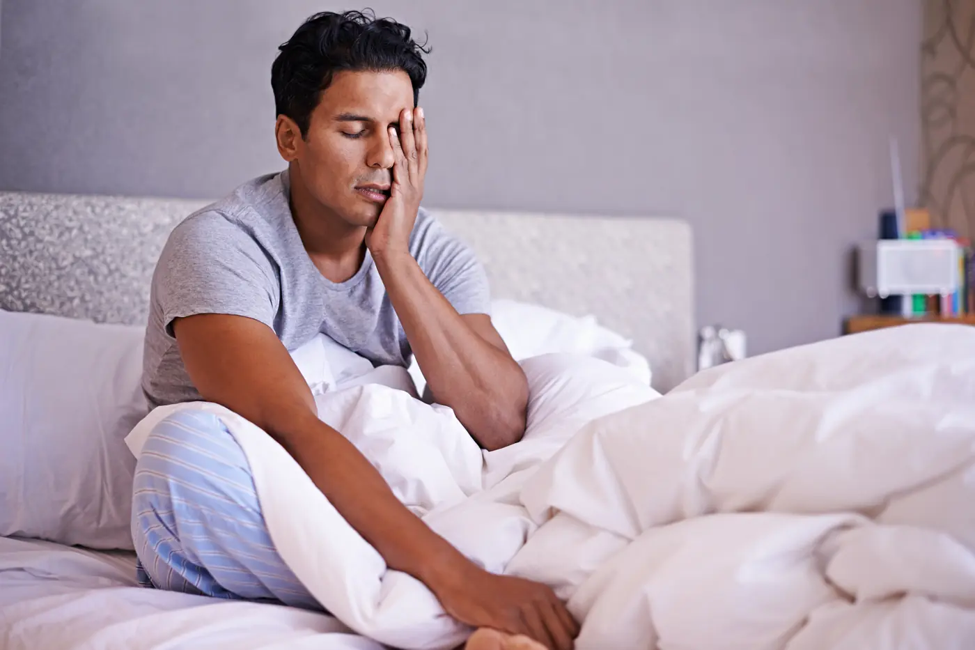 Man sitting up in bed with a morning migraine.