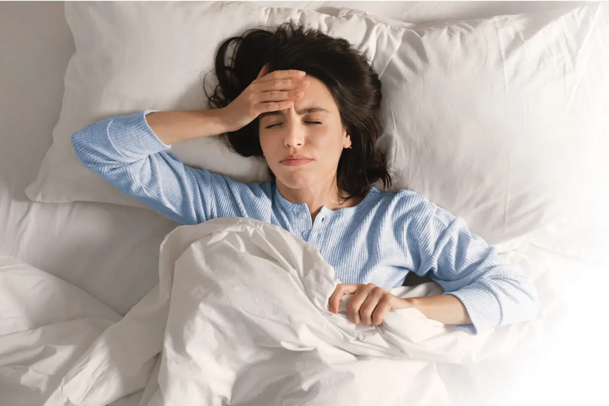 Woman lying in bed with a morning migraine.